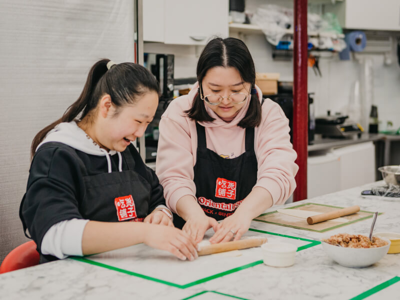 Teacher helping a cookery student to shape dough in a dumpling making class